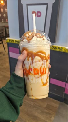 a person holding up a drink with chocolate and caramel on it in front of a sign