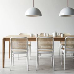 a dining room table with four chairs and two lamps above it, all in white