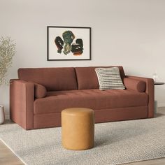 a living room with a couch, ottoman and coffee table in front of a painting on the wall