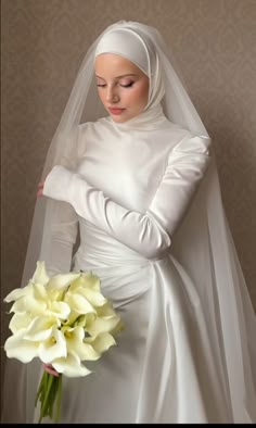 a woman in a white wedding dress holding a bouquet of flowers and wearing a veil