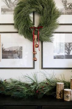 a christmas wreath is hanging on the wall above a mantle with evergreen branches and bells