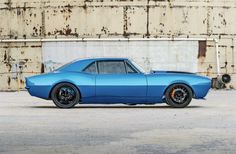 a blue muscle car parked in front of an old building with rusted metal walls