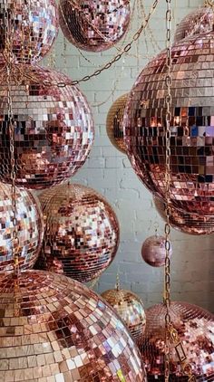 many shiny disco balls hanging from chains in front of a brick wall