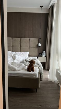 a teddy bear sitting on top of a bed in a bedroom next to a window