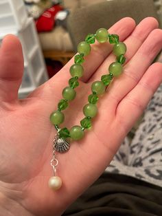 a person is holding a green beaded necklace in their hand with a bell charm on it