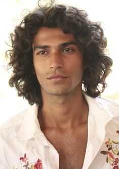 a man with long curly hair wearing a white shirt and flowered collarless shirt