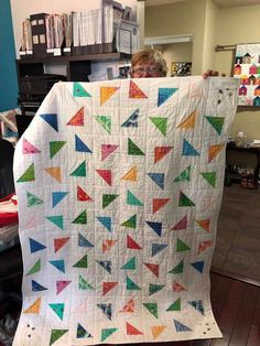 a woman holding up a quilt made with triangles