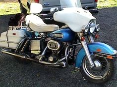 a blue and white motorcycle parked in front of a car with a dog sitting on the back seat