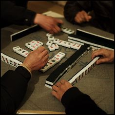 several people playing dominos on a table with their hands in the middle of them