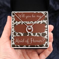 a hand holding a box with a necklace on it that says, will you be my maid of honor?