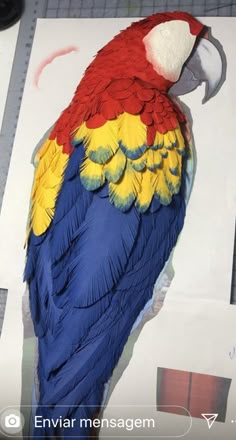 a paper mache of a colorful parrot sitting on top of a piece of paper