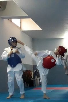 two young men practicing martial moves in an indoor gym area with blue mats and white walls