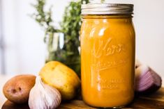 a jar filled with yellow liquid next to garlic and potatoes