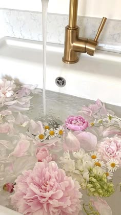 pink and white flowers are floating in a sink with water running from the faucet