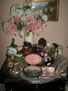 a table topped with pink and white flowers next to a vase filled with lots of stuff