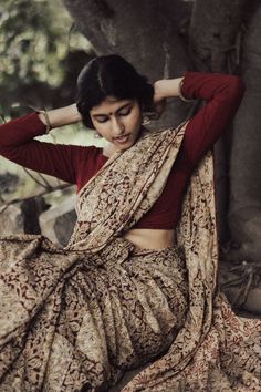 a woman sitting on the ground with her hands behind her head wearing a sari