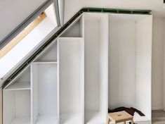 a room with white walls and open shelving units on the floor next to a wooden stool