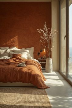 a bedroom with an orange colored wall and white bedding, along with a large window overlooking the ocean