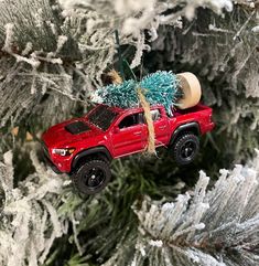 a red truck ornament hanging from a christmas tree with frost on it's branches