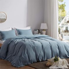 a bed with blue comforters and pillows in a white room next to a window