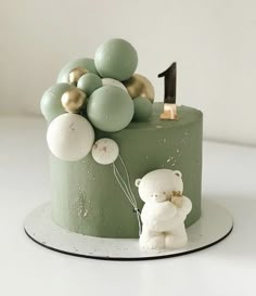 a green cake with balloons and a teddy bear on it's side, sitting on a plate