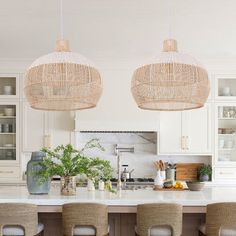 a kitchen with white cabinets and wicker pendant lights above the island countertop, surrounded by beige chairs