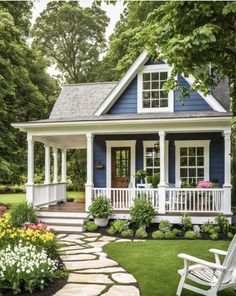 a small blue house with white porches and flowers in the front yard, surrounded by grass