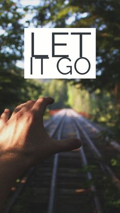 a person's hand holding up a sign that says let it go on the train tracks