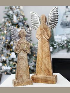 two wooden angel figurines sitting on top of a table next to a christmas tree