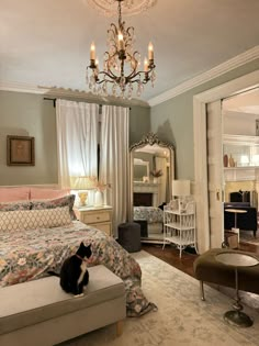 a cat sitting on top of a bed next to a dresser in a room with a chandelier