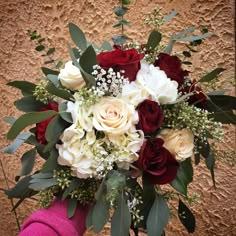 a bridal bouquet with roses and greenery in front of a brown stucco wall