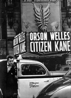 an old black and white photo of a man standing next to a car in front of a theater