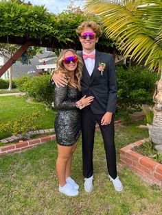 a man in a tuxedo standing next to a woman wearing sunglasses and a sequin dress