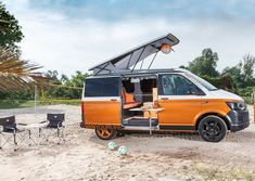 an orange van is parked in the sand with its roof open and it's door open