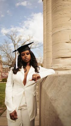 a woman in a graduation cap and gown leaning against a column with her hand on her hip