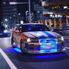 two cars driving down the road at night with blue lights on their hoods and headlights