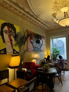 a woman sitting at a table in a room with paintings on the wall