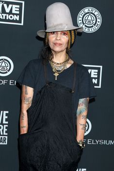 a woman with tattoos and a hat on posing for the camera in front of a black backdrop