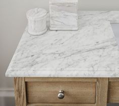 a white marble counter top next to a wooden drawer with a tissue dispenser on it