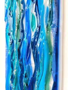 blue and green glass art piece hanging on the side of a white wall in front of a window