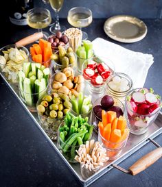 an assortment of vegetables are arranged on a platter with utensils and wine glasses