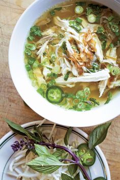 two bowls filled with soup and vegetables on top of a wooden table next to each other