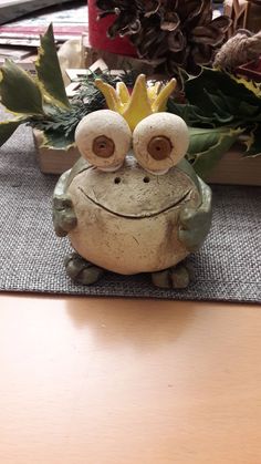 a ceramic frog sitting on top of a wooden table next to potted plants and pine cones