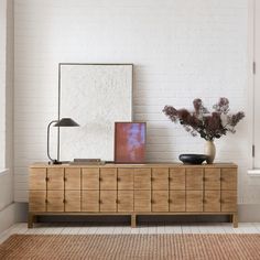 a vase with flowers and a mirror on top of a dresser in a white room