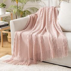 a pink blanket sitting on top of a white couch next to a potted plant