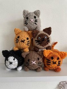 a group of small crocheted cats sitting on top of a white shelf next to each other