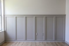 an empty room with white paneling and wood floors