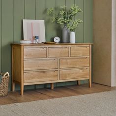 a wooden dresser with flowers and pictures on it in a green painted room, next to a wicker basket