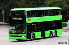 a green double decker bus driving down the street with people on it's side