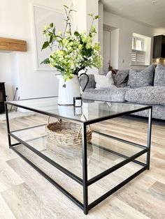 a glass coffee table with flowers on top in a living room area next to a couch